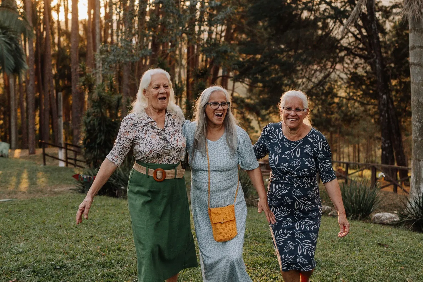 Três amigas de mais de 60 anos caminhando juntas num parque ao entardecer