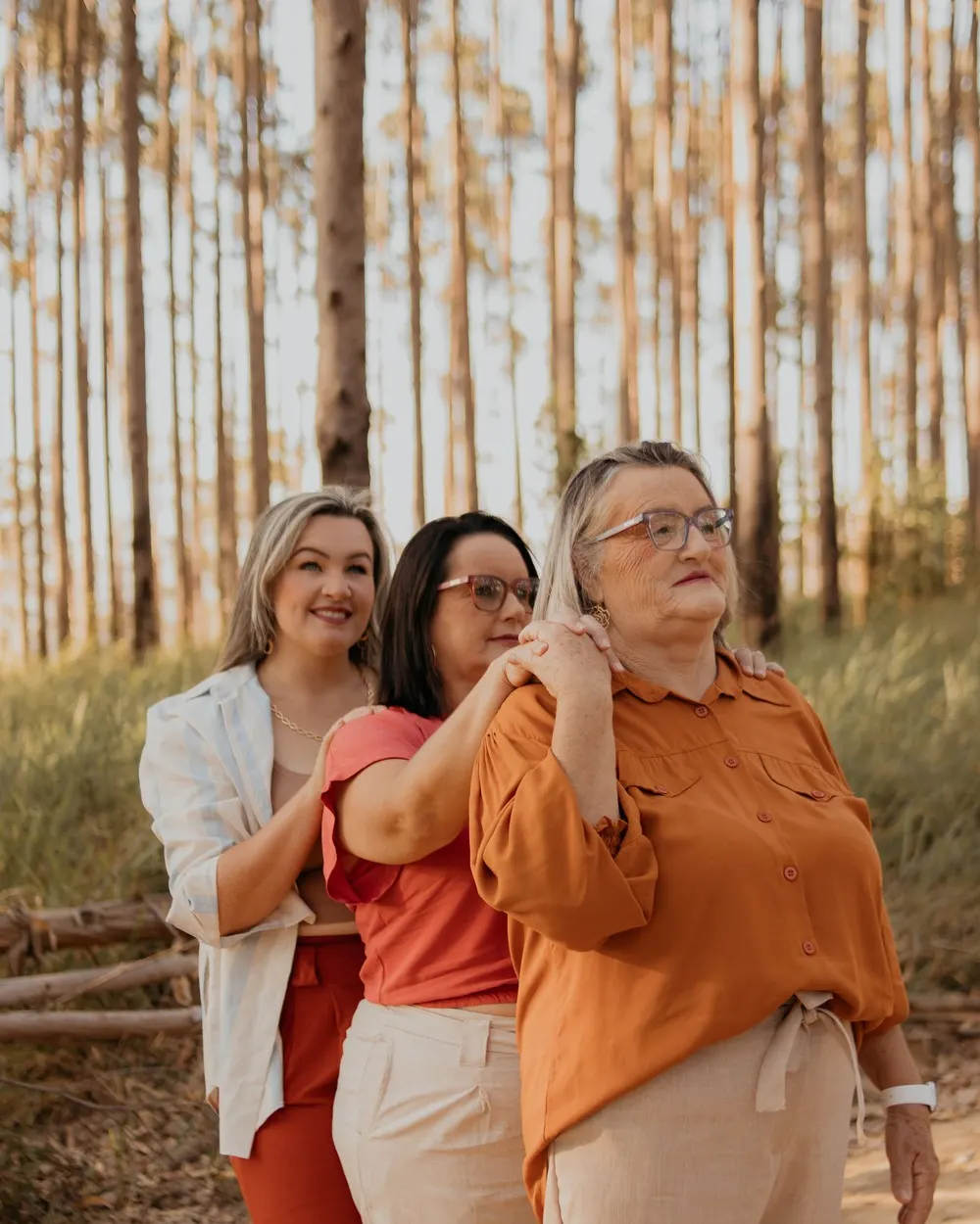 Três mulheres de gerações diferentes sorrindo juntas num bosque